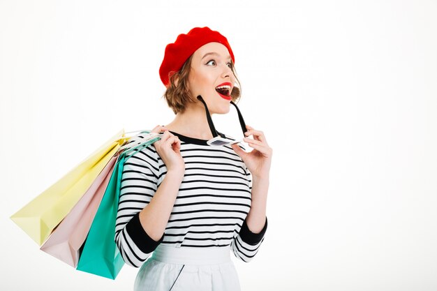 Surprised ginger woman with packages and sunglasses looking away over grey