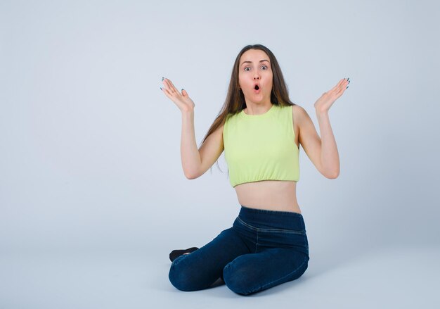 Surprised girl is opening wide her hands by sitting on floor on white background