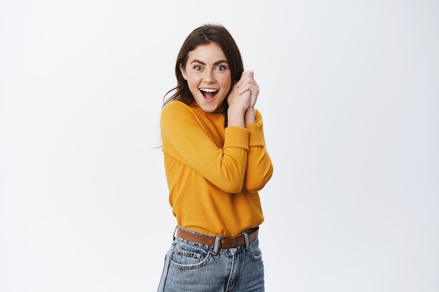 Surprised girl receive interesting offer, gasping amazed and happy, holding hands pressed to body and smiling at front, staring at prize, white wall