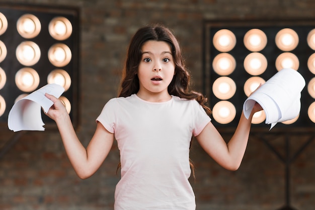 Surprised girl standing in front of stage light holding scripts