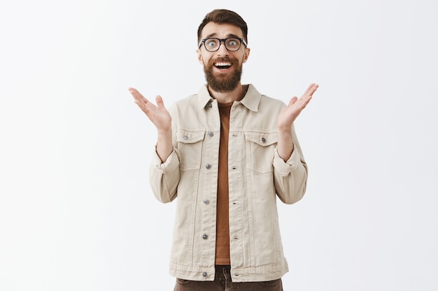 Surprised and grateful bearded man in glasses posing against the white wall