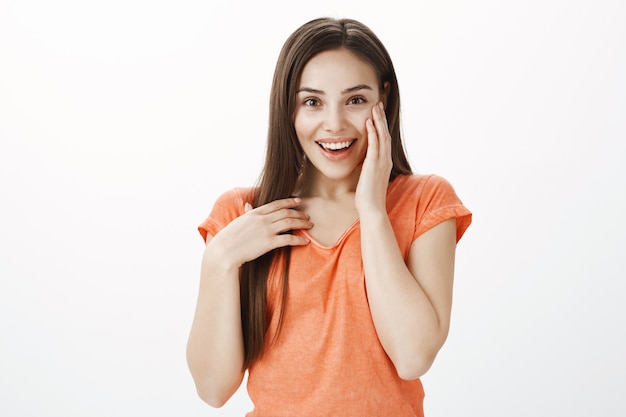 Surprised and grateful cute brunette girl holding hands on heart, looking glad or thankful