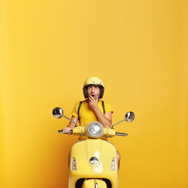 Ragazzo sorpreso con il casco che guida il motorino giallo