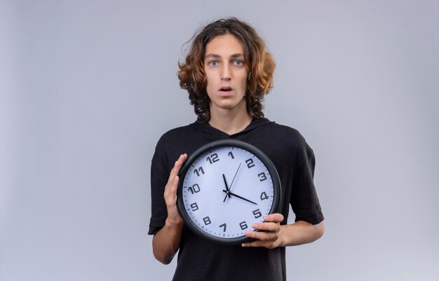 Surprised guy with long hair in black t-shirt a wall clock on white background