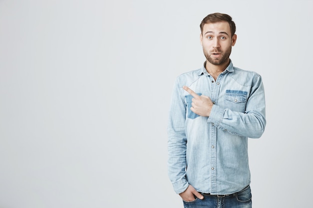 Surprised handsome bearded guy pointing finger left