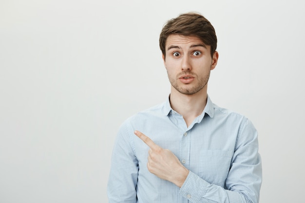 Free photo surprised handsome guy pointing finger upper left corner at advertisement