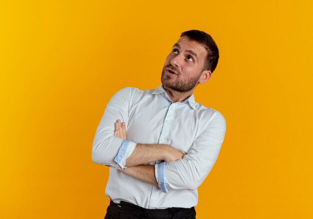 Surprised handsome man crosses arms looking up isolated on orange wall