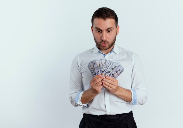 Surprised handsome man holds and looks at money isolated on white wall