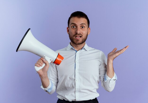 Surprised handsome man holds loud speaker isolated on purple wall