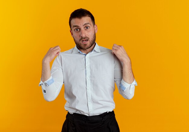 Surprised handsome man holds shoulders looking isolated on orange wall