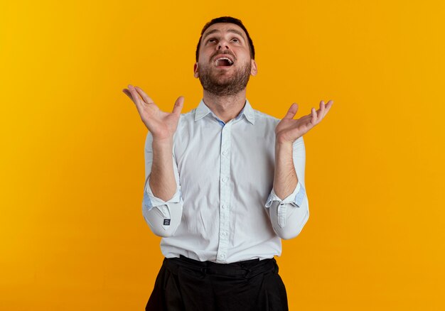 Surprised handsome man looks up with raised hands isolated on orange wall