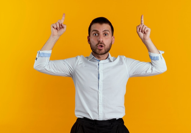 Surprised handsome man points up with two hands looking isolated on orange wall