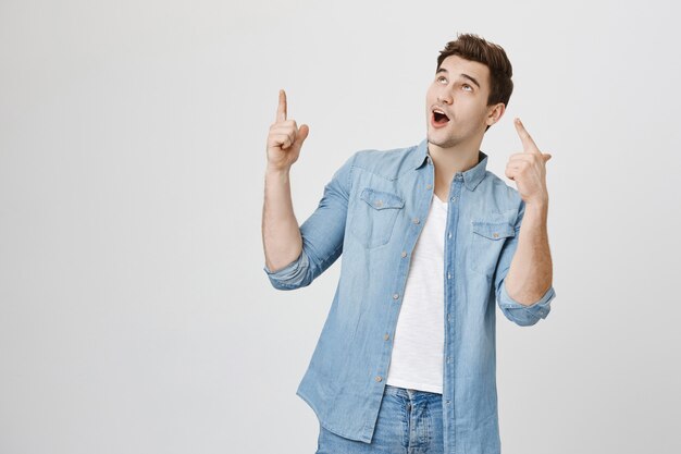 Surprised handsome man showing banner, pointing up