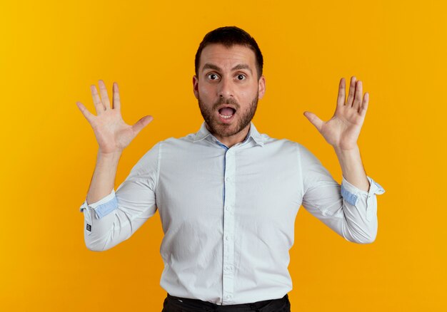 驚いたハンサムな男は、オレンジ色の壁に隔離された両手を上げて立っています
