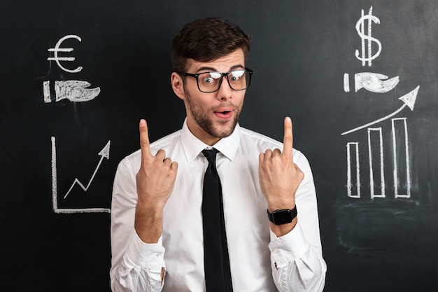 Surprised handsome young man in glasses pointing with two fingers upward