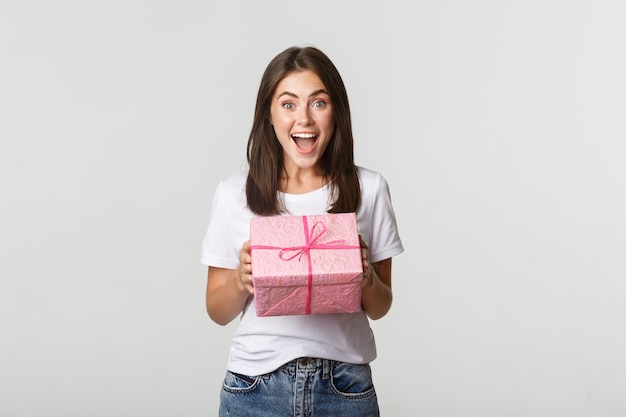 Удивленная девушка с днем рождения получает обернутый подарок, белый.