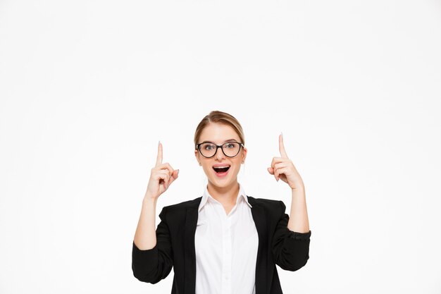 Surprised happy blonde business woman in eyeglasses pointing up