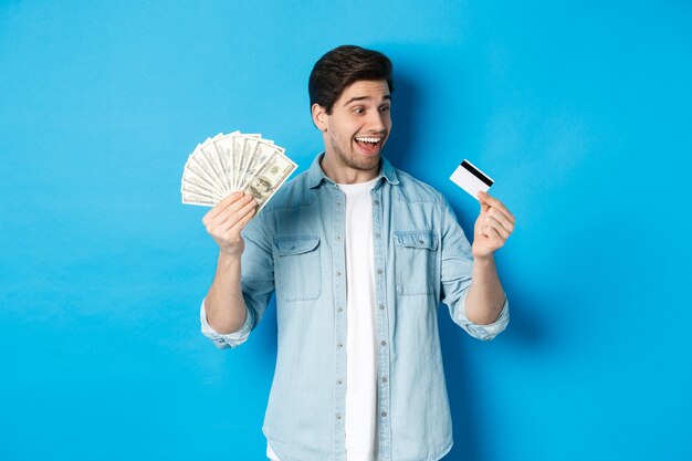 Surprised and happy man looking at credit card and showing money, concept of bank loan, finance and income.