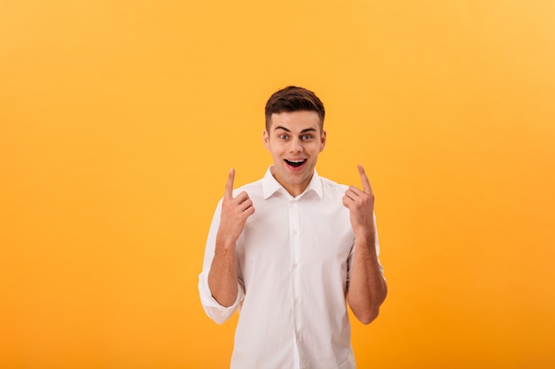 Surprised happy man in white shirt pointing up and looking at the camera
