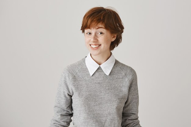 Surprised and happy redhead girl with short haircut posing against the white wall