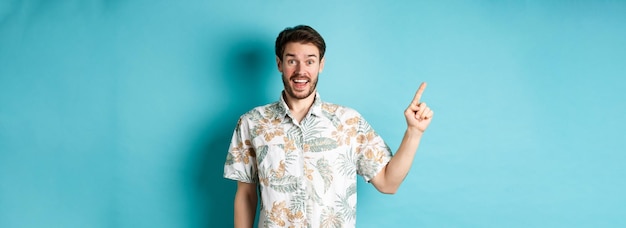 Бесплатное фото Удивленный счастливый турист, указывающий пальцем на пустое место, показывает крутое промо, стоящее на гавайском языке