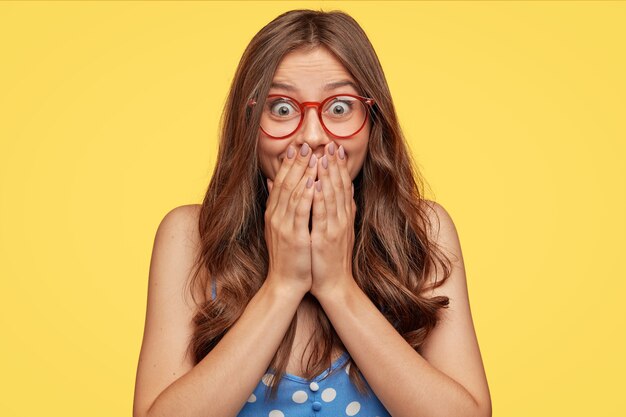 Surprised happy young girl looks with happiness at camera, cant believe in unexpected triumph or success, covers mouth with both hands