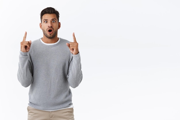 Surprised hispanic bearded man with stylish modern hairstyle open mouth wondered gasping fascinated with admiration pointing up impressed with incredible sale product features white background