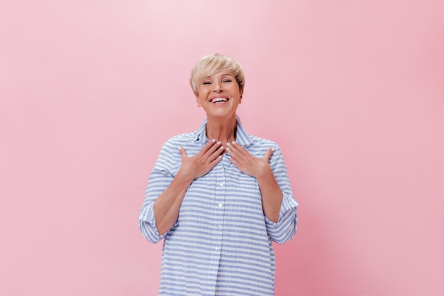 Surprised lady in blue outfit happily looks into camera on pink background