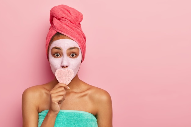 驚いた女性は、ハート型のスポンジで口を覆い、化粧を落とし、若く見えるように顔に粘土マスクを適用し、頭に包まれたタオルを着用します
