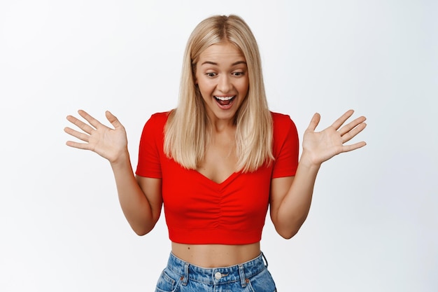 Free photo surprised laughing girl looks down shaking hands and smiles amazed stands against white background