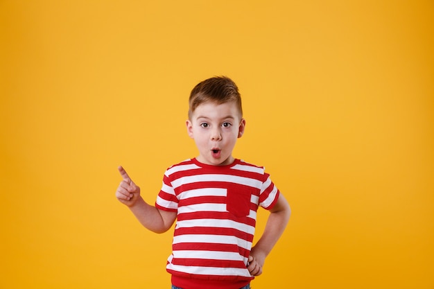 Surprised little boy standing and pointing finger away