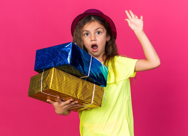복사 공간 핑크 벽에 고립 제기 손으로 서 선물 상자를 들고 보라색 파티 모자와 놀란 된 어린 백인 소녀