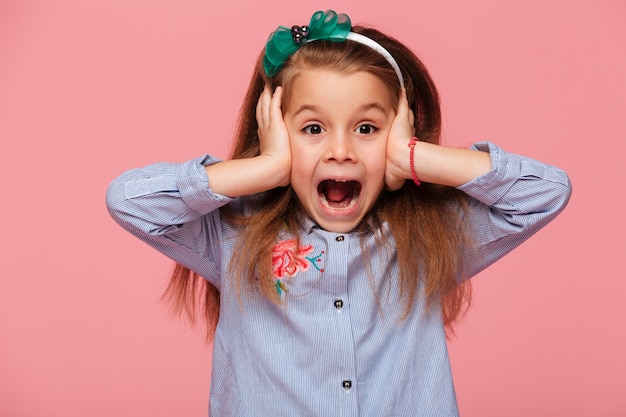 Free photo surprised little girl covering her ears with both hands not listening or overhearing screaming with open mouth