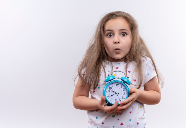 Free photo surprised little school girl wearing white t-shirt holding alarm clock on isolated white background