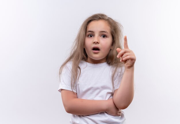 Surprised little school girl wearing white t-shirt points to up on isolated white background