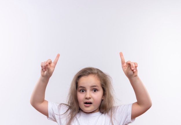 Surprised little school girl wearing white t-shirt points to up on isolated white background