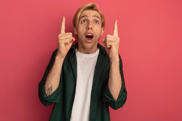 Surprised looking up young blonde guy wearing green t-shirt points at up