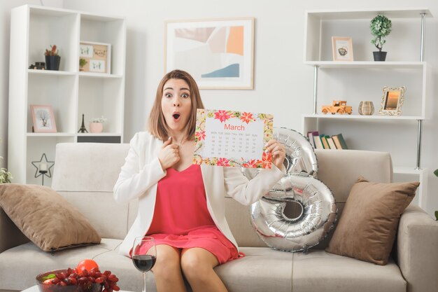 Surprised looking woman on happy women's day holding calendar sitting on sofa in living room