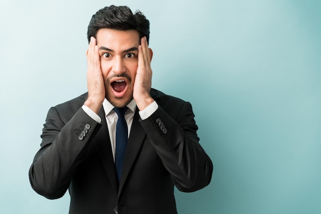 Surprised male entrepreneur making eye contact with head in hands against colored background