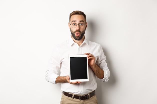 Surprised man in glasses, showing digital tablet screen, looking amazed, standing  