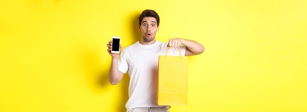 Free photo surprised man holding shopping bag and showing smartphone screen concept of mobile banking and app a