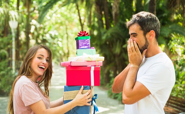 Free photo surprised man looking at his girlfriend holding stack of gifts