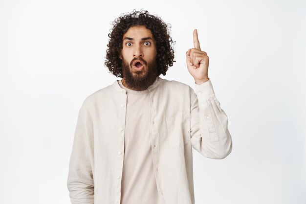 Surprised middle eastern man pointing finger up looking impressed showing advertisement white background