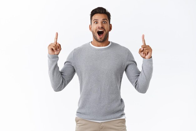 Surprised overwhelmed young hispanic handsome man open mouth fascinated stare popped eyes wondered pointing up to promote incredible promo offer standing white background impressed