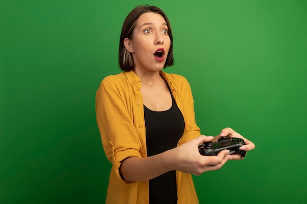 Surprised pretty caucasian woman holds controller on green