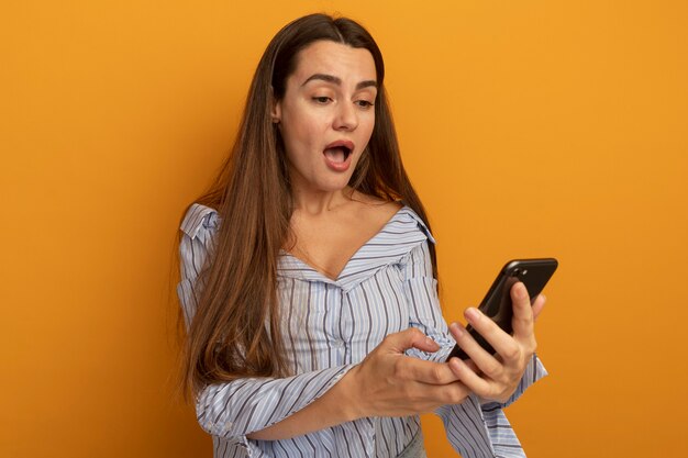 Surprised pretty caucasian woman holds and looks at phone isolated