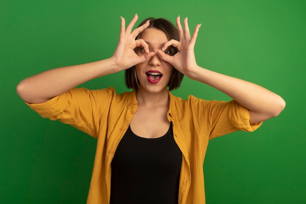 Surprised pretty caucasian woman looks at camera through fingers on green