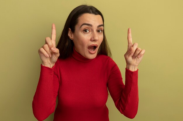 Surprised pretty caucasian woman points up with two hands isolated