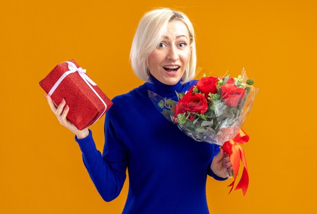 Удивленная симпатичная славянская женщина, держащая букет цветов и подарочную коробку на день святого валентина