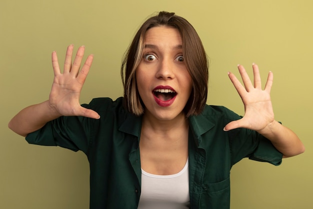 Foto gratuita la donna graziosa sorpresa sta con le mani alzate isolate sulla parete verde oliva